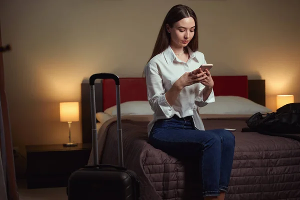 部屋のベッドに座っている間 魅力的な女性が電話を参照してください ホテルのチェックイン — ストック写真