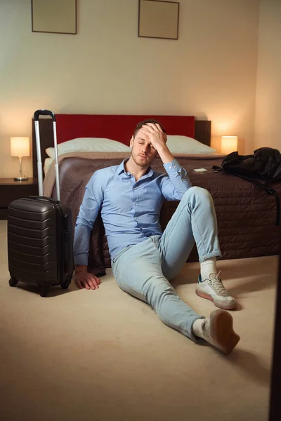 厌倦了的年轻男性坐在酒店房间的床上 双手放在头上 — 图库照片