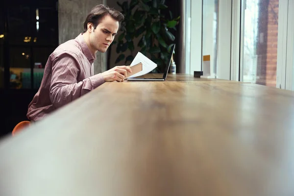 Mężczyzna Dokumentem Ręku Wpatrujący Się Ekran Smartfona Siedząc Laptopie Kawiarni — Zdjęcie stockowe