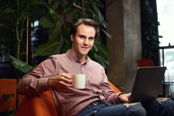 Lächelnder Junger Mann Mit Keramiktasse Der Hand Und Laptop Sessel — Stockfoto