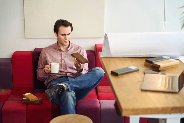 オフィスの木材サンプルを見てソファの上に座っ手でカップと深刻な焦点を当てたインテリアデザイナー — ストック写真