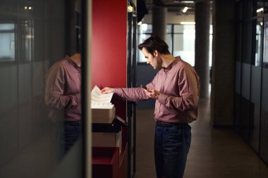 Elinde akıllı telefon olan odaklanmış şirket çalışanı, fotokopi makinesinin belge besleyicisine kağıt yerleştiriyor