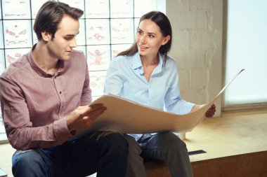 Genç mimari takımı ahşap bankta otururken katın planlarını tartışıyor.