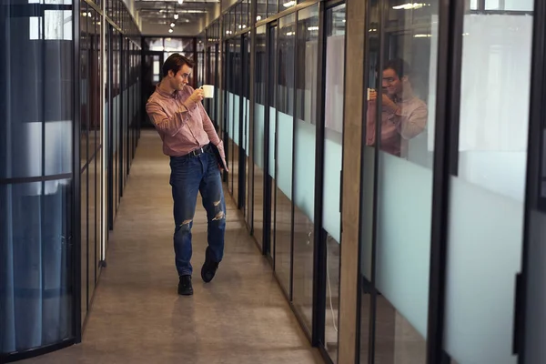 男ノートパソコン歩く廊下に沿って彼の反射を歓迎しながらガラスの壁に手でティーカップ — ストック写真