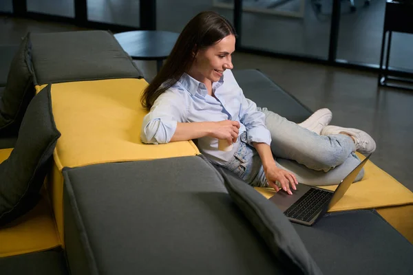 Wanita Ceria Menggunakan Komputer Portabelnya Sambil Duduk Sofa Ruang Tunggu — Stok Foto