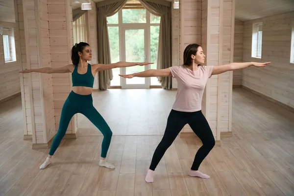 穿着运动服的年轻女性朋友站在一起 在房间里表演瑜伽 — 图库照片