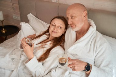 Evli çift ellerinde bir fincan kahveyle yatakta hayal kuruyor.