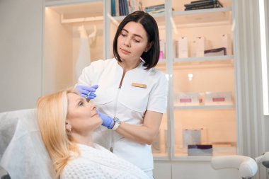 Kozmetik uzmanı güzellik salonundaki olgun kadın yüzünde pürüzleri gidermek için canlandırıcı iğne yapıyor.