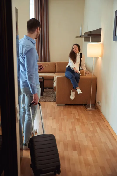 Happy Lady Sitting Sofa Hotel Room Looking Man Suitcase Check — Stock Photo, Image