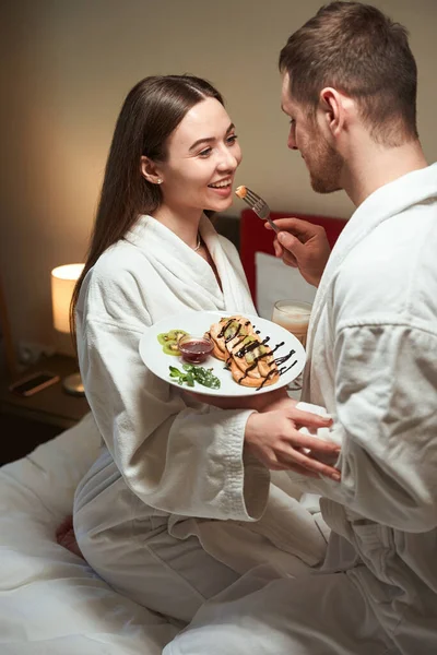男人在床上用美味的早餐招待他快乐的年轻妻子 — 图库照片