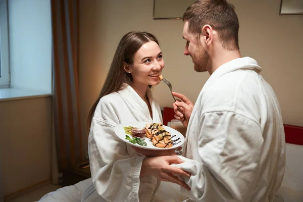 有爱心的男性在床上用美味的煎饼招待快乐的年轻女性伴侣 — 图库照片