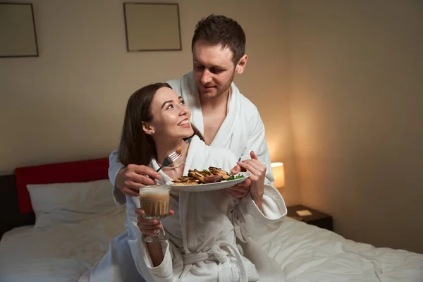 Caring Young Man Feeding Smiling Female Spouse Tasty Fritters Bed — Stock Photo, Image