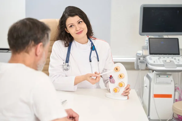 Beyaz Önlüklü Kadın Kardiyolog Masada Oturuyor Klinikteki Adama Kalp Modelini — Stok fotoğraf