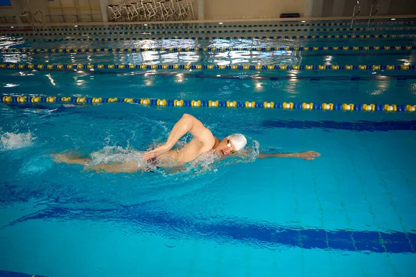 头戴白帽 戴护目镜的成年男子在游泳池游泳 — 图库照片