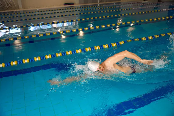 身穿白帽和护目镜的成年运动员在游泳池游泳 — 图库照片