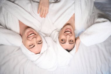 Beyaz bornozlu iki bayanın vücut tedavisinden ve kahkahalardan memnun bir şekilde yatakta yatışının en üst görüntüsü.