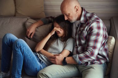 Önemseyen ebeveyn üzgün ergen kızının yanında, kanepede oturuyor.