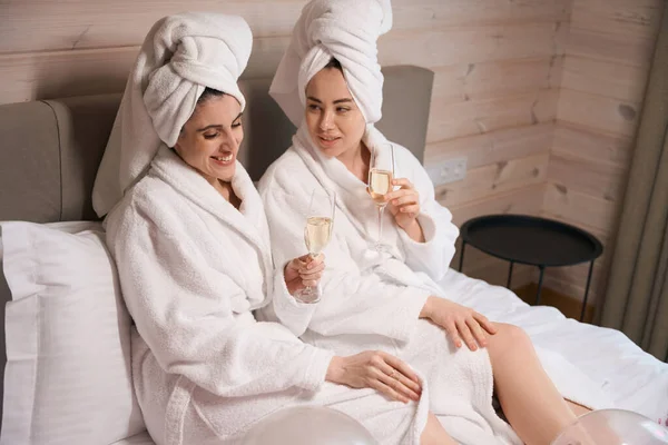 Two Ladies Wearing Bathrobes Lying Big Bed Hotel Room Talking — Stock Photo, Image