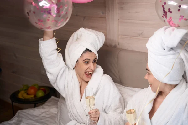 Dvě Radostné Dámy Balónky Sklenicemi Šampaňského Sedící Velké Posteli Smějící — Stock fotografie