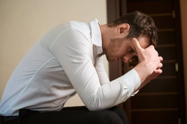 Düşüncelere dalmış odada yalnız oturan üzgün adamın yan görüntüsü.