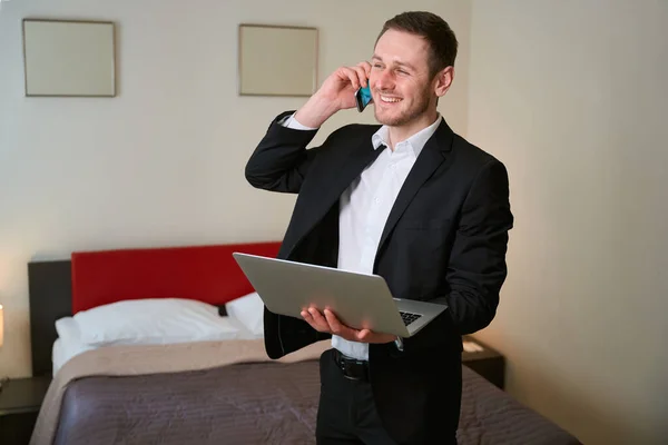 Wesoły Facet Laptopem Ręku Podczas Rozmowy Telefonicznej Luksusowym Apartamencie — Zdjęcie stockowe