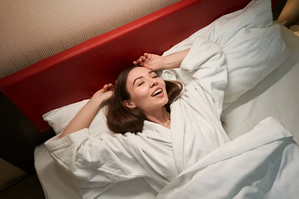 穿着浴衣的快乐年轻女人睡在舒适的床上 柔软的枕头上 — 图库照片