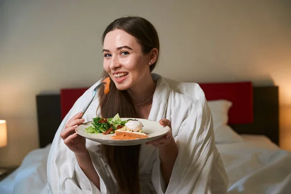 ウエストアップポートレートの楽しい女性ラップで毛布を持って朝食ながらベッドに座ってスイート — ストック写真