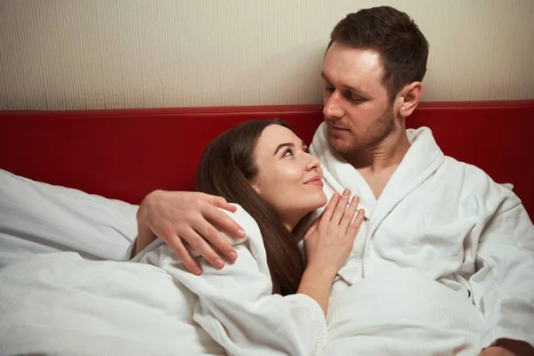 在酒店房间里 一个浪漫的男人抱着一个年轻女人躺在床上 — 图库照片