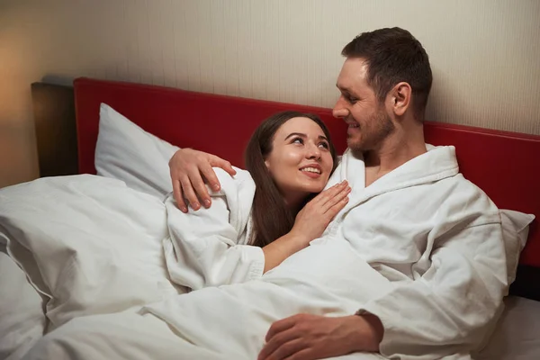 一个可爱的男人抱着他快乐的女伴躺在床上躺在套间里 — 图库照片