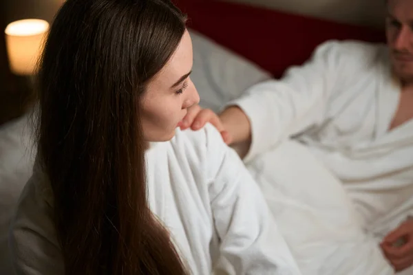 穿着浴衣的男人躺在舒适的床上拍拍他的女伴的肩膀 — 图库照片