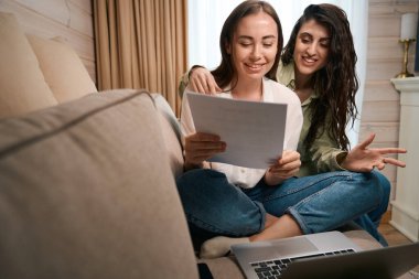 Akıllı bayanlar rahat bir oturma odasında kanepede oturup bilgisayarlarını kullanarak evlerinden uzakta çalışıp belgeleri inceleyip analiz ediyorlar.