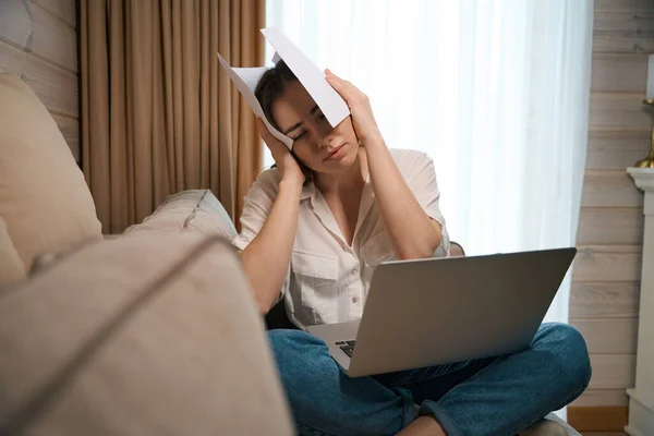 疲惫的年轻女士在笔记本电脑上工作 坐在沙发上 用手捂住脸 感觉头痛偏头痛 — 图库照片