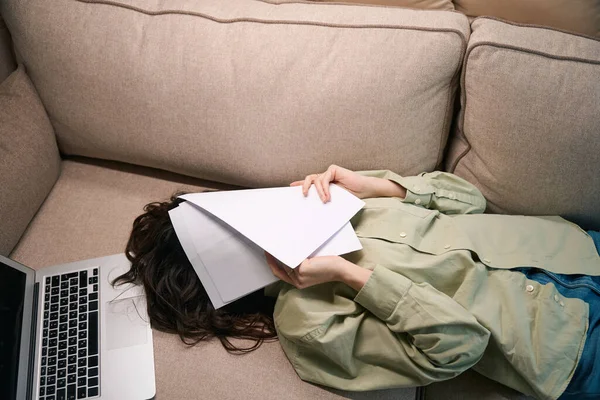疲惫的年轻女士躺在沙发上 躺在笔记本电脑上 用手捂住脸 感觉头痛偏头痛 — 图库照片