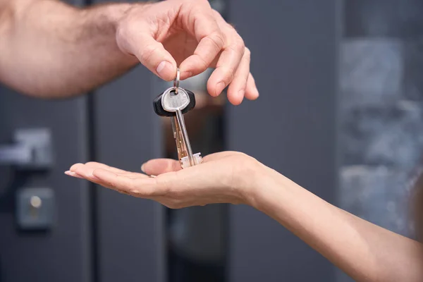 Mans hand gives the keys to the womans hand on the background of the house