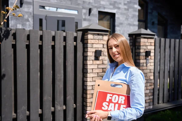 Kaukasische Junge Immobilienmaklerin Auf Dem Hintergrund Des Hauses Blickt Lächelnd — Stockfoto