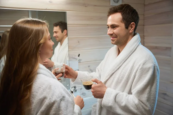 Morning with coffee in bathroom, a man gives a woman a cup of coffee