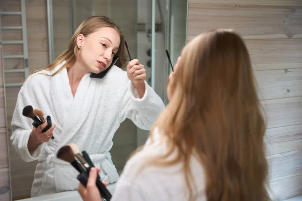 Giovane Signora Che Parla Smartphone Applicando Mascara Simultaneamente Vicino Specchio — Foto Stock