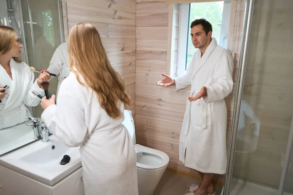 Mladá Žena Dává Make Koupelně Blízkosti Zrcadla Muž Stojí Okna — Stock fotografie