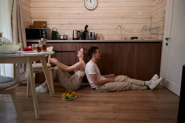 男人和女人背对着背坐在厨房的地板上 — 图库照片