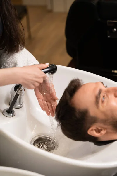 Female washes the head of a client at a special sink, male in a protective cape