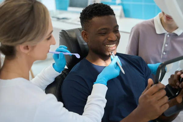 女牙医用镰刀探头向男性病人展示她治疗和修补的牙齿位置 非洲裔美国病人对医生的工作感到满意 — 图库照片