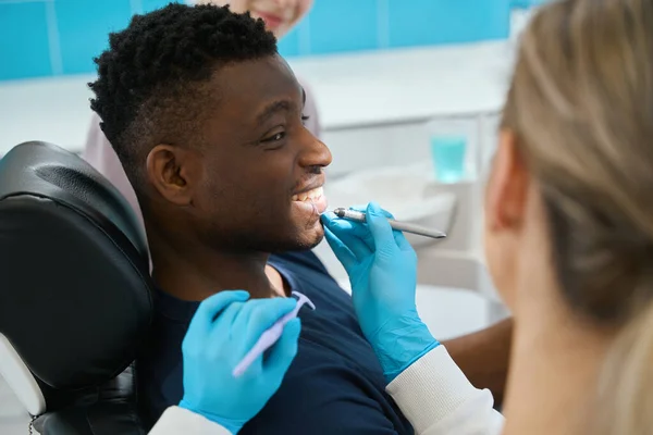 笑顔のアフリカ系アメリカ人男性は 病気の探査機で歯の健康をチェックし 完全に彼の医者に信頼している女性の症候学者を見ています — ストック写真