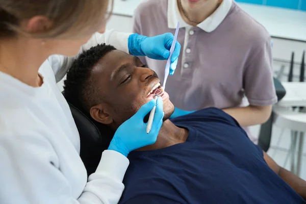 若い男性の歯 定期的な検査および処置 専門の歯のクリーニングの健康を点検する口ミラーを見る女性の病理学者 — ストック写真