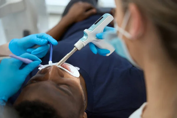 近距离女性口腔科医生给非洲裔美国人注射局部麻醉注射器 护士协助保持唾液喷射器 — 图库照片