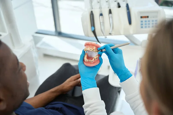 男性の患者に彼の問題の歯を示し 治療方法 各クライアントへの特別なアプローチを説明する顎のモックアップを保持する女性の物理学者 — ストック写真