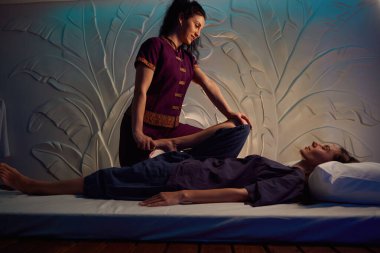 Gülümseyen masöz, sakin bayan müşterinin eğilmiş bacağını göğsüne doğru itiyor.