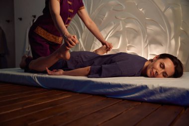 Masöz ayaklarını gluteus 'a doğru bastırırken rahatlamış kadın müşteri şiltenin üzerinde yatar.