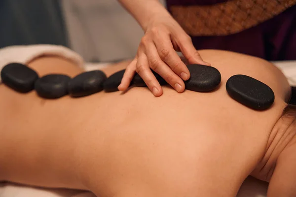 Stock image Cropped photo of spa therapist placing hot stones on naked back of patient