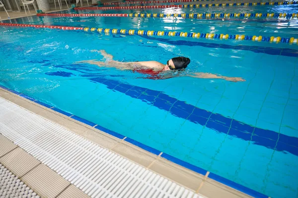 穿着护目镜和泳帽的年轻女运动员在水里爬行 — 图库照片