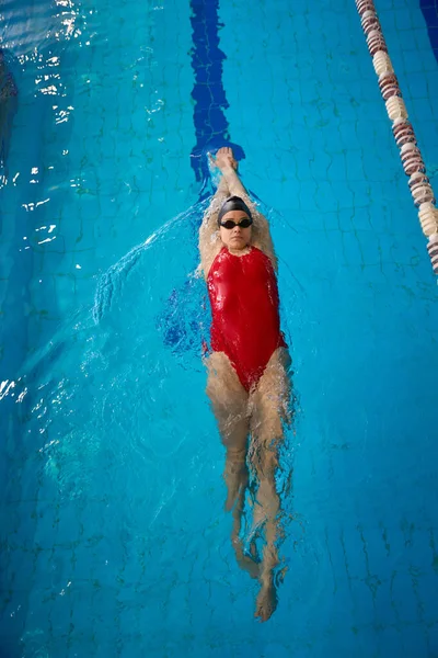 一个戴着泳帽和护目镜的严肃的年轻女运动员在水里漂浮着 — 图库照片